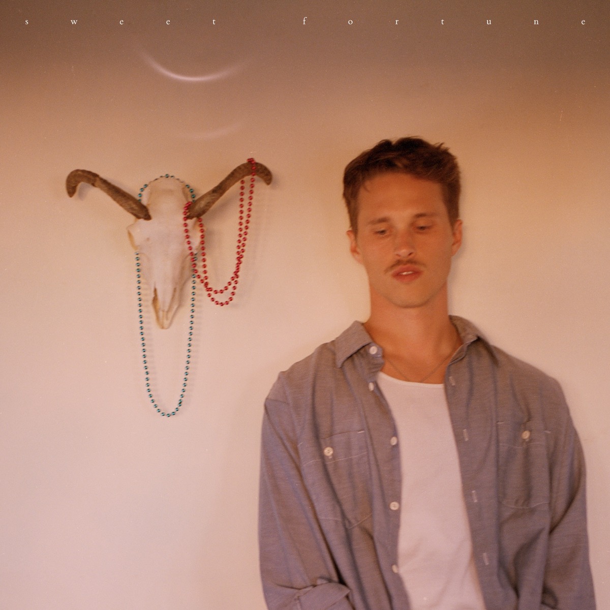 Ryan Beatty stands beside a horned animal skull decorated with colorful beads against a softly lit wall